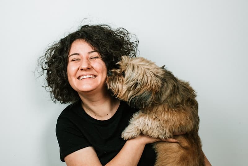 A woman laughing as a small terrier licks her face